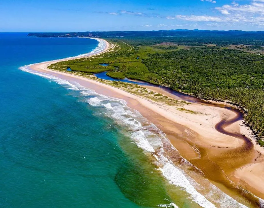 Vista aérea de uma praia de Itacaré, com mar azul-esverdeado, faixa de areia, rio e mata preservada