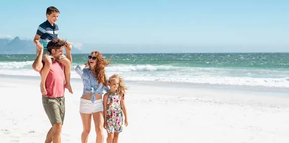 Família caminhando na praia: pai com o filho nos ombros, mãe e filha