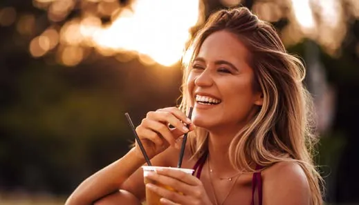 Mulher sorrindo enquanto toma uma bebida ao entardecer
