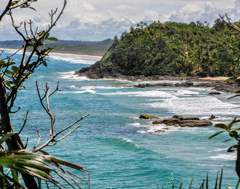 Costa de Itacaré com ondas, rochas e morro coberto de mata tropical