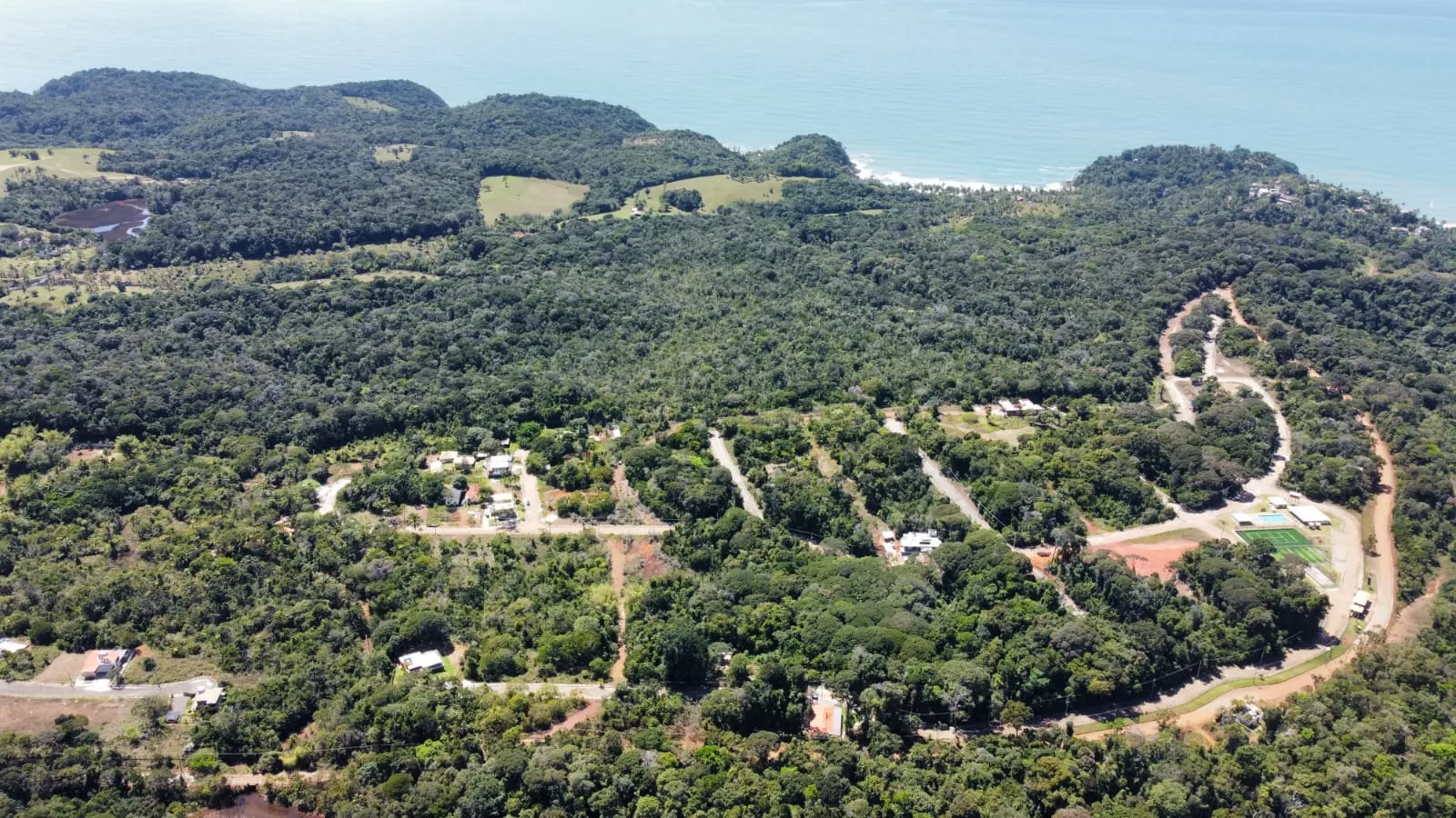 Vista aérea ampla mostrando as vias internas, as casas já construídas e o mar ao fundo